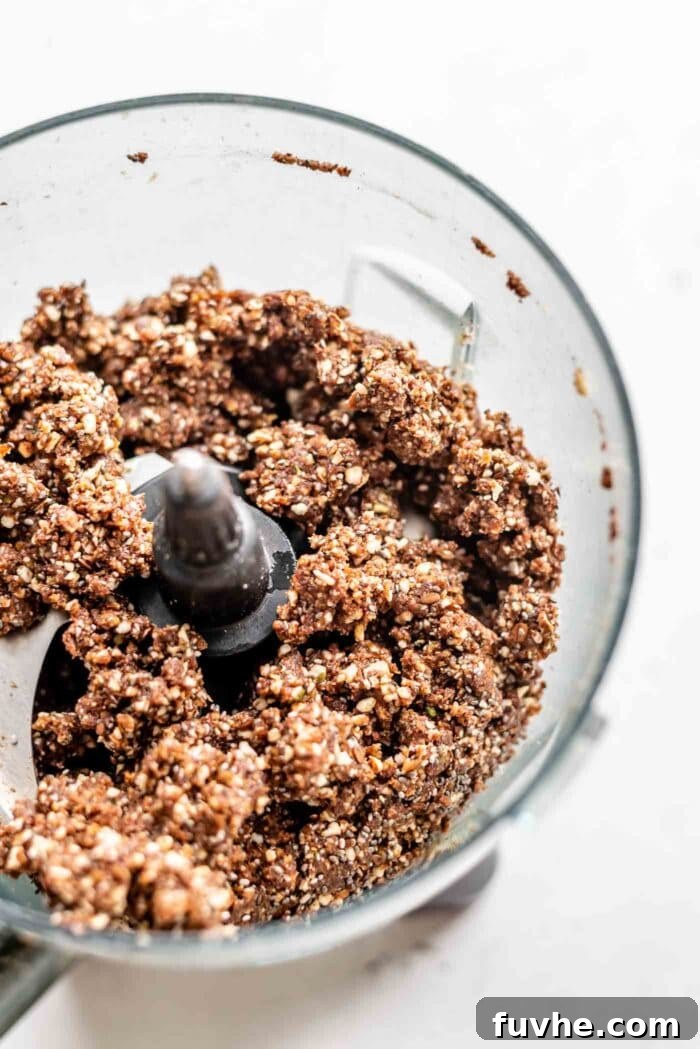 The no-bake chocolate energy bar dough, sticky and well-formed, inside a food processor bowl.