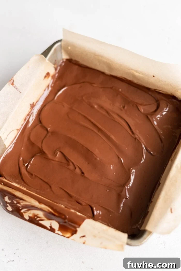 Melted chocolate generously spread over the energy bars in a small baking pan, ready to be chilled.