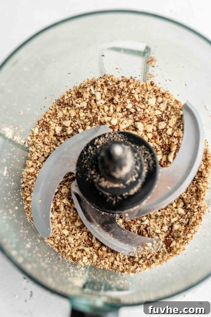 Blended nuts in a food processor, showing a coarse, flour-like consistency with some small pieces visible.
