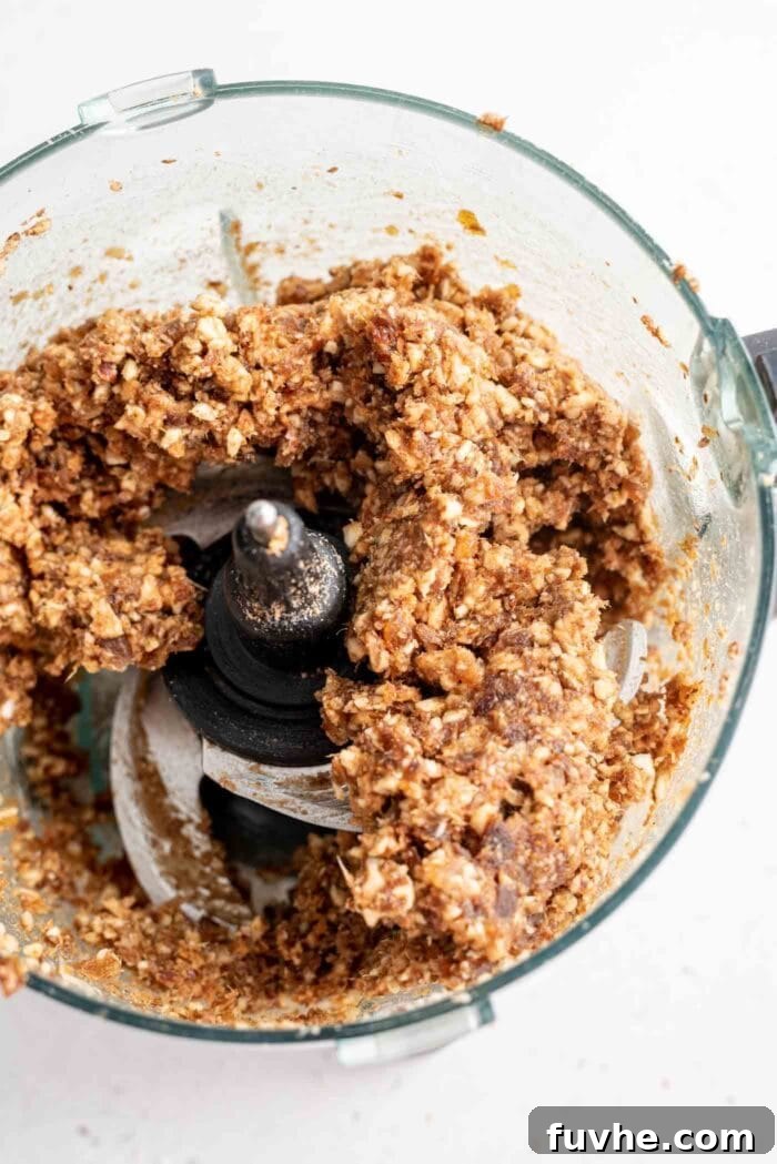 Raw energy ball dough in a food processor, appearing thick and sticky, ready for shaping.