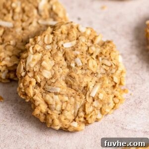 A coconut oatmeal cookie resting on another cookie with a few more cookies scattered around it.