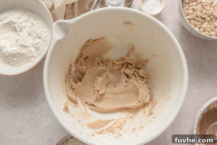 Softened vegan butter and brown sugar expertly creamed together in a spacious mixing bowl, exhibiting a light and fluffy texture, ready for the next step in the cookie preparation.