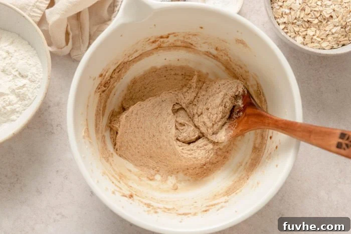 The creamy mixture of butter and sugar in a mixing bowl, with the flax egg and vanilla extract recently added, being thoroughly combined with a wooden spoon.