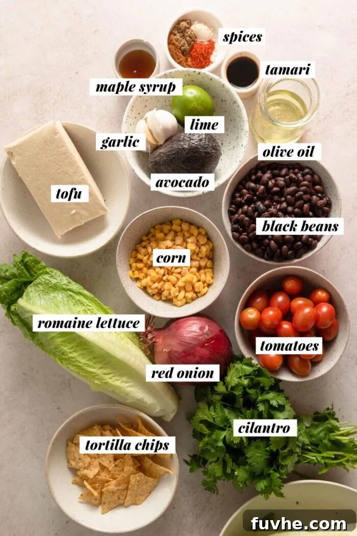 A vibrant collection of fresh, raw ingredients laid out on a clean surface, including blocks of tofu, various vegetables, beans, corn, and components for the dressing, ready to be prepared for a delicious vegan Santa Fe salad.