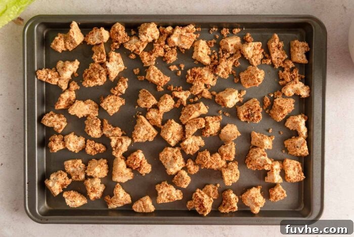 Close-up of crispy, browned tofu bits coated in a savory spice blend, spread out evenly on a baking sheet, showcasing their ready-to-eat perfection.