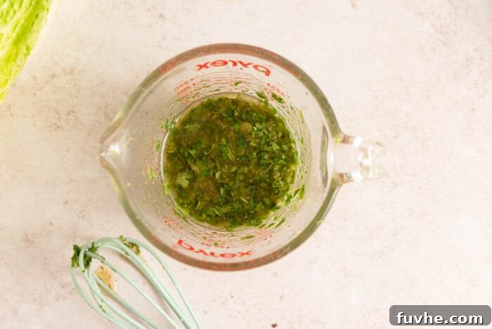 Freshly prepared cilantro lime vinaigrette glistening in a glass measuring cup, with a whisk resting beside it, indicating its readiness to dress the salad.