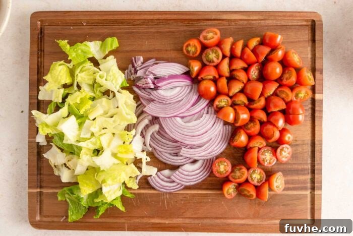 A trio of freshly chopped vegetables for the Santa Fe salad—juicy cherry tomatoes, crisp romaine lettuce, and thinly sliced red onion—neatly arranged on a rustic wooden cutting board, awaiting assembly.