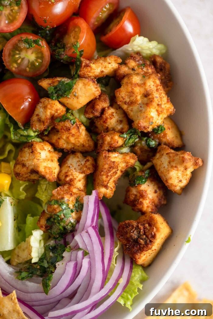 Close-up of golden crispy, browned tofu pieces beautifully nestled within a vibrant Santa Fe salad, alongside tender red onion, fresh green lettuce, and juicy red tomatoes in a serving bowl, ready to be enjoyed.