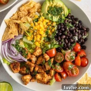 Overhead view into a healthy vegan Santa Fe salad bowl, beautifully arranged with golden crispy tofu, sweet corn, creamy avocado slices, hearty black beans, juicy cherry tomatoes, and thinly sliced red onion, all garnished with crumbled tortilla chips.