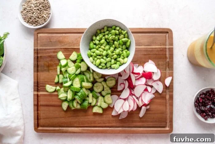 Chopped cucumber and radish on a cutting board with a bowl of shelled edamame beans.
