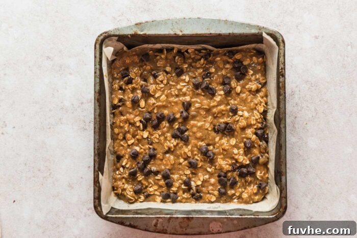 Wholesome Vegan Oatmeal Bars 7 Raw chocolate chip oatmeal cookie bars batter in a baking dish lined with parchment paper.