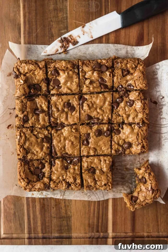 Wholesome Vegan Oatmeal Bars 9 Overhead view of a batch of chocolate chip oatmeal cookie bars cut into 16 squares on a cutting board. One bar is pulled out and has a bite taken out of it.