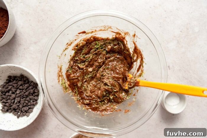 Raw zucchini brownie batter in a mixing bowl with a yellow spatula resting in it.