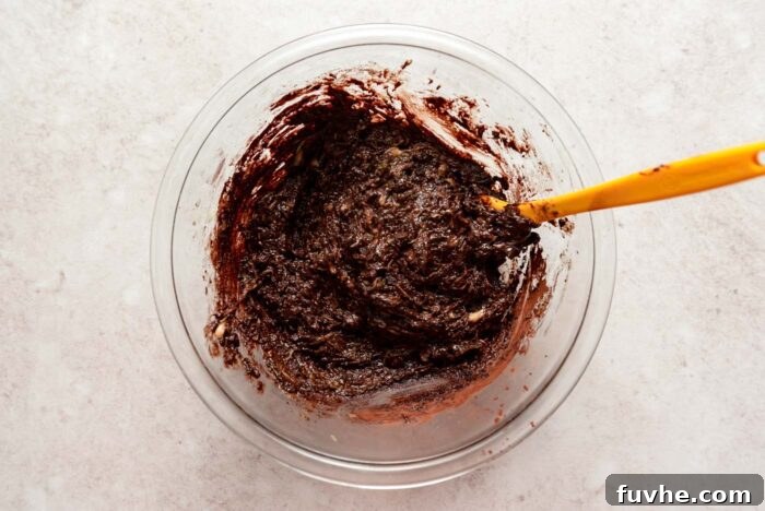 Thick zucchini brownie batter with chocolate chips mixed together in a mixing bowl with a spatula.