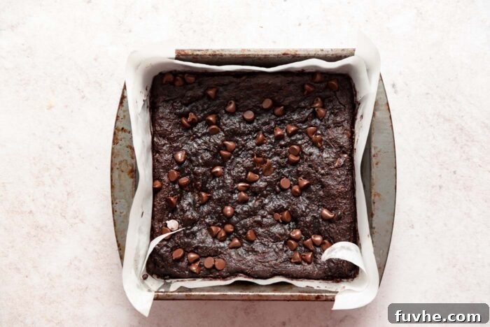 A baking pan of brownies sprinkled with chocolate chips. The pan is lined with parchment paper.