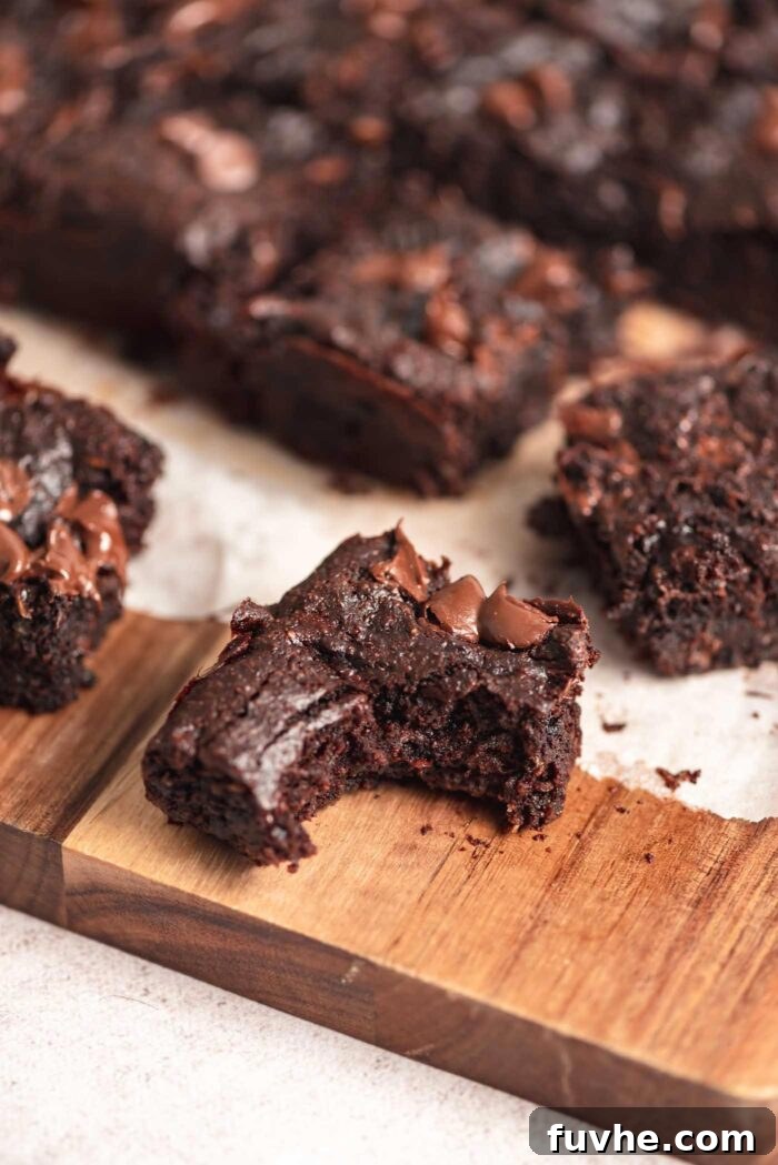 A chocolate chip zucchini brownie with a bite out of it on a cutting board with more brownies in the background.