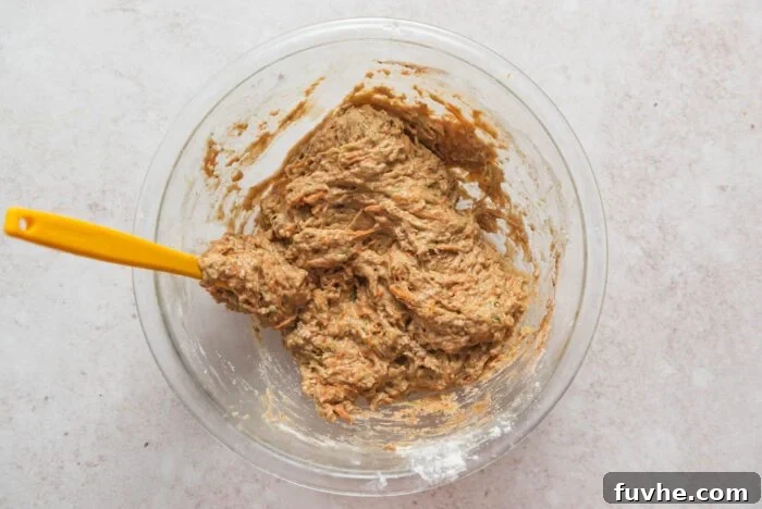 The full raw carrot and zucchini muffin batter, perfectly mixed in a large bowl, with a wooden spoon resting in it.