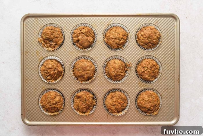 A dozen perfectly baked carrot zucchini muffins nestled in a muffin pan, golden brown and ready to enjoy.