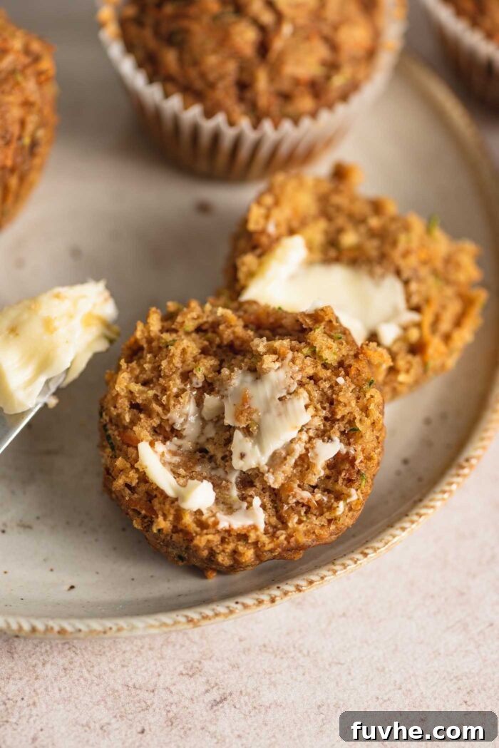 A healthy vegan carrot zucchini muffin, beautifully cut in half and generously spread with butter, presented on a simple plate.