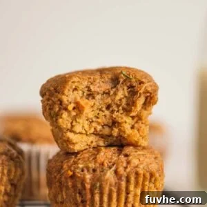 Two carrot zucchini muffins stacked on one another. The muffin on top has a bite out of it so you can see the texture and bits of grated carrot and zucchini inside.