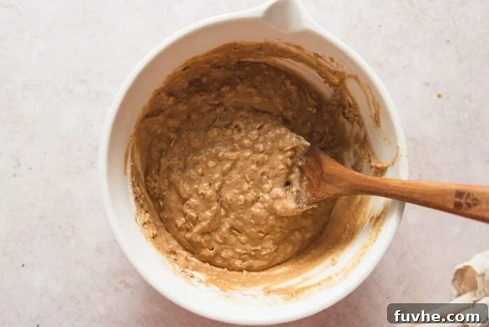 Raw oatmeal muffin batter in a mixing bowl with a wooden spoon resting in it.