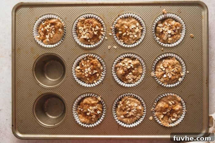 10 unbaked oatmeal muffins in paper liners in a muffin pan. Each muffin is sprinkled with rolled oats.