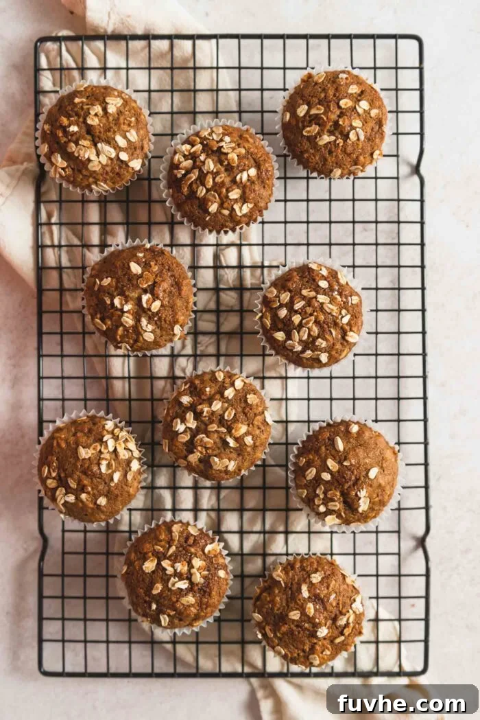 10 oatmeal muffins sitting on a wire baking cooling rack over a dish cloth. Each muffin has a few rolled oats sprinkled on top.