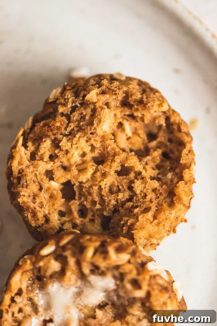 A torn open oatmeal muffin on a plate. One half of the muffin has a spread of butter melting on it.