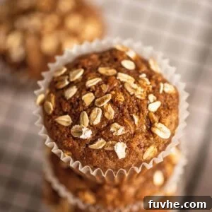 A stack of 3 oatmeal muffins in paper liners on the edge of a baking cooling rack.