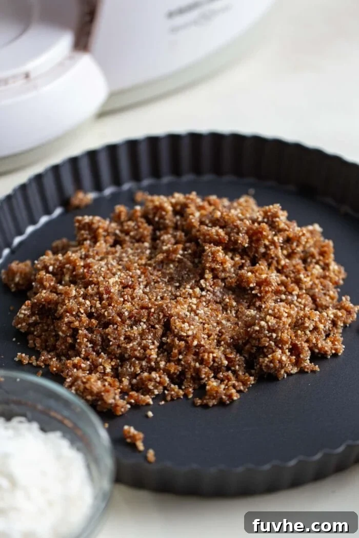 A close-up view of the freshly prepared, crumbly no-bake raw pie crust, pressed neatly into a small pie dish, showcasing its rustic texture.