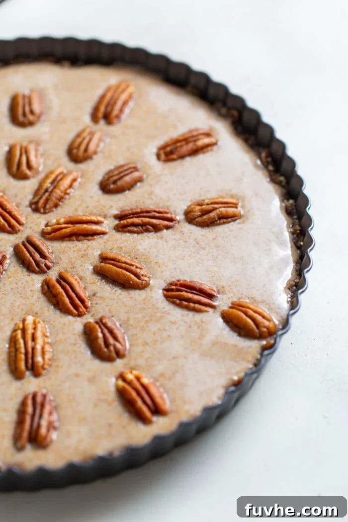 The raw vegan maple pecan pie, beautifully set in its dish and artfully topped with whole pecans, ready to be sliced and served.