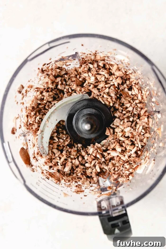 Roughly chopped mushrooms being processed in a food processor to achieve a fine, even dice, illustrating the first step in preparation.