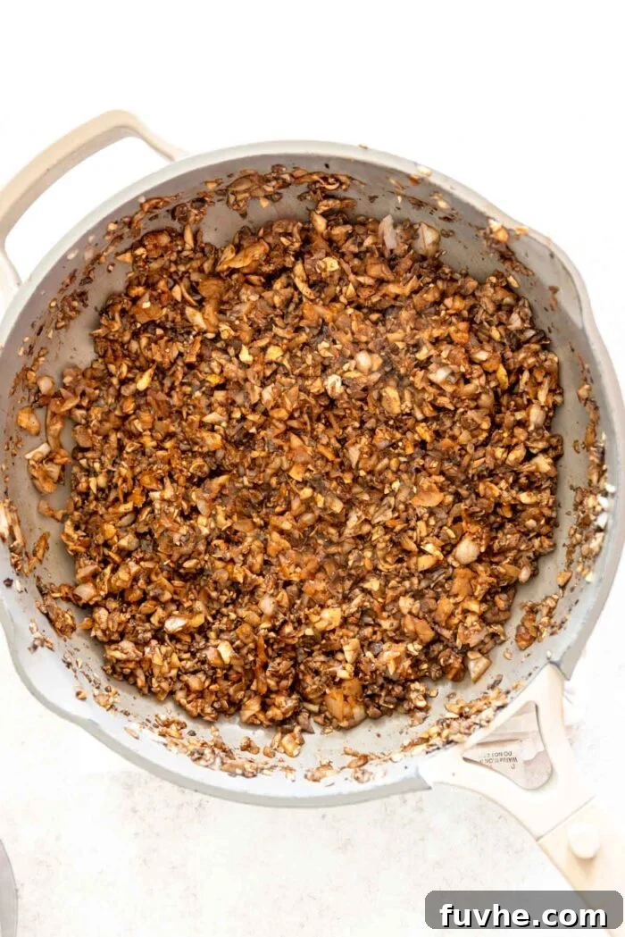 Finely diced mushrooms and onions cooking in a skillet with a blend of spices, releasing their moisture and building savory aromas.