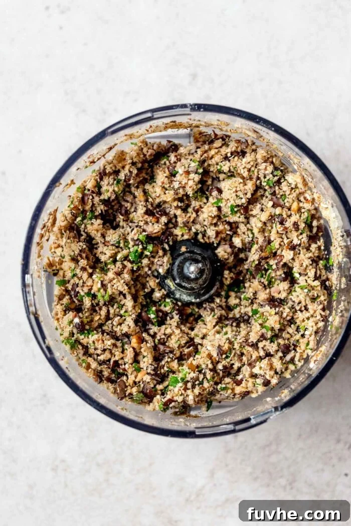 The food processor bowl now containing the previously blended dry ingredients, along with drained black beans, BBQ sauce, and tamari, ready for a final pulse.