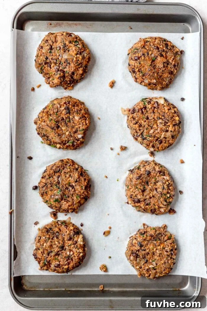 Eight uniformly shaped mushroom veggie burger patties neatly arranged on a parchment paper-lined baking sheet, ready for the oven.