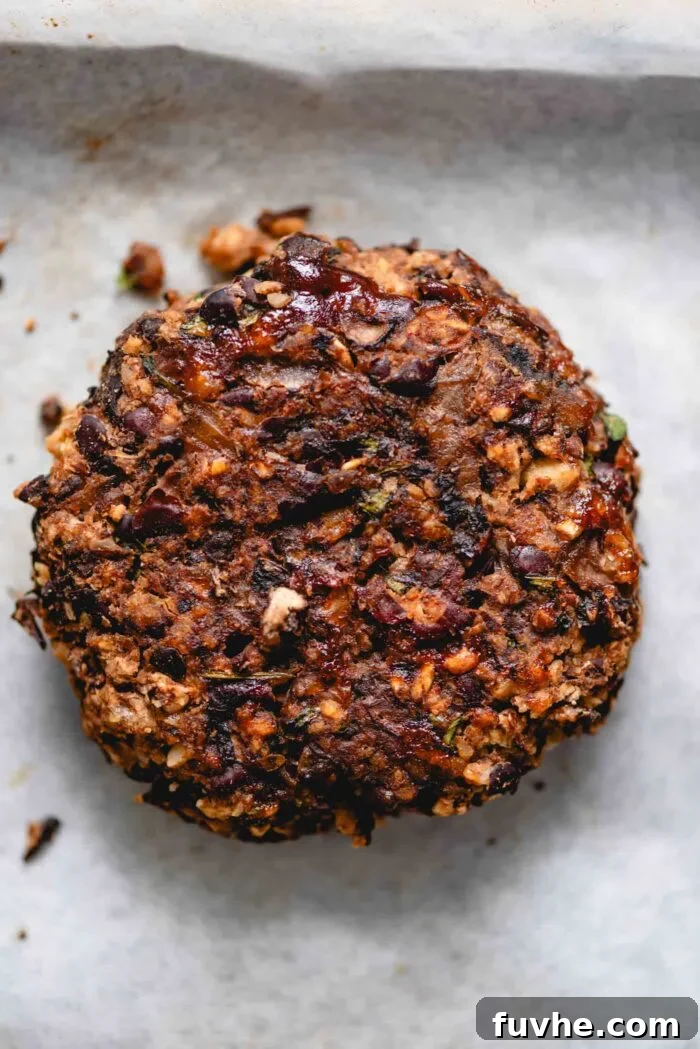 A single baked black bean veggie burger patty resting on a parchment paper-lined baking sheet, showcasing its firm, golden-brown texture after cooking.