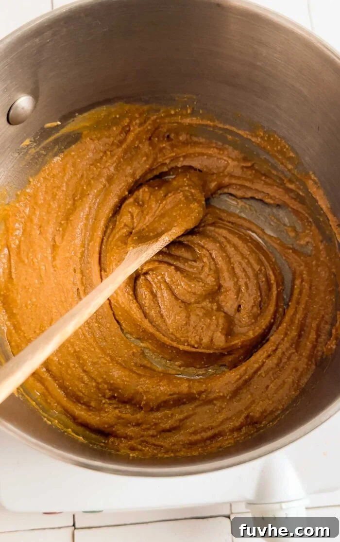 Peanut butter and maple syrup cooking in a small pot with a wooden spoon on it.