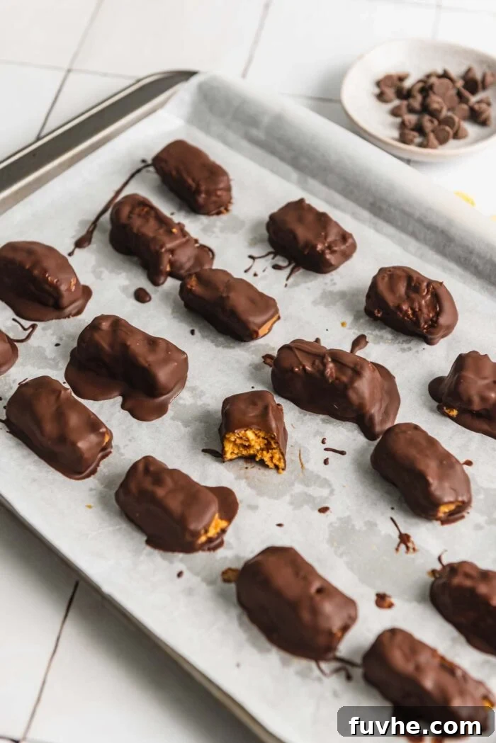 A baking sheet of homemade butterfinger candy bars. One bar has a bite out of it so you can see the texture inside.