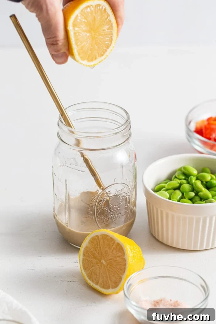 Hand squeezing half a lemon into a jar of tahini.