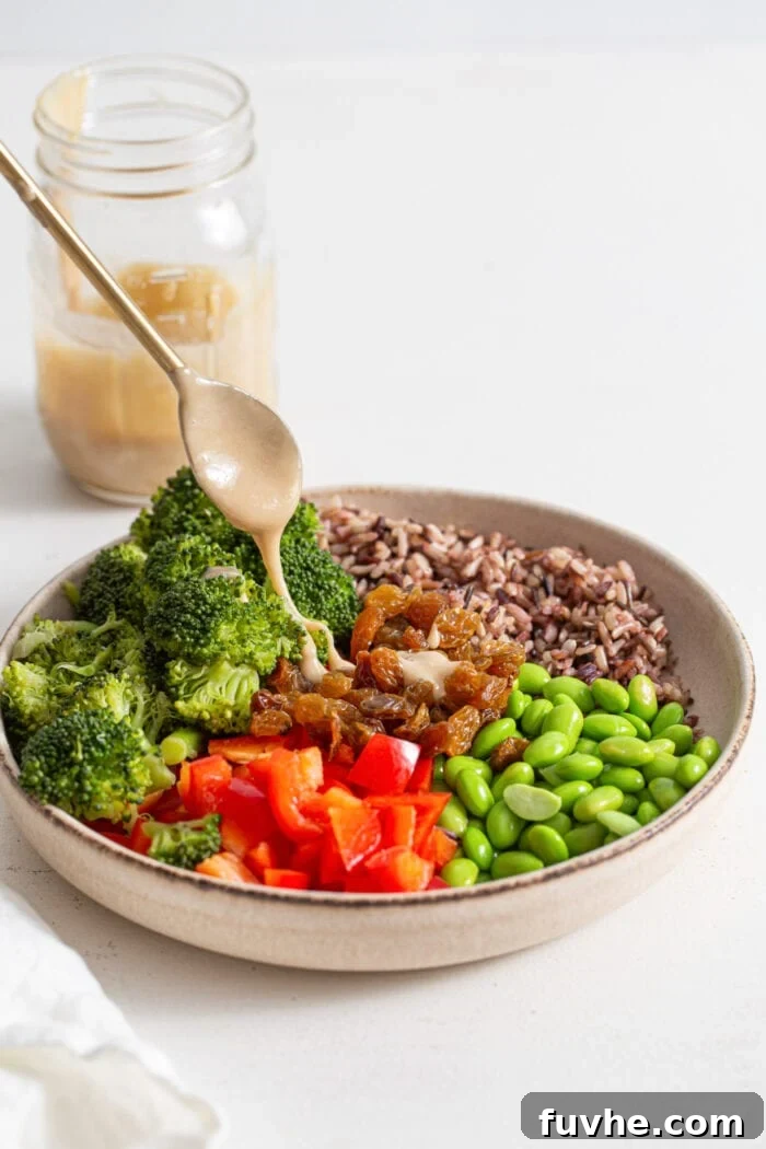 Drizzling a spoonful of tahini dressing over a large bowl of chopped vegetables, edamame and wild rice.