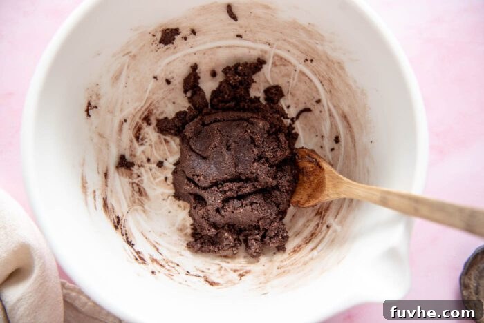 Raw chocolate cookie dough in a glass mixing bowl with a spoon resting in it, ready for chilling before being shaped into homemade vegan Thin Mints.