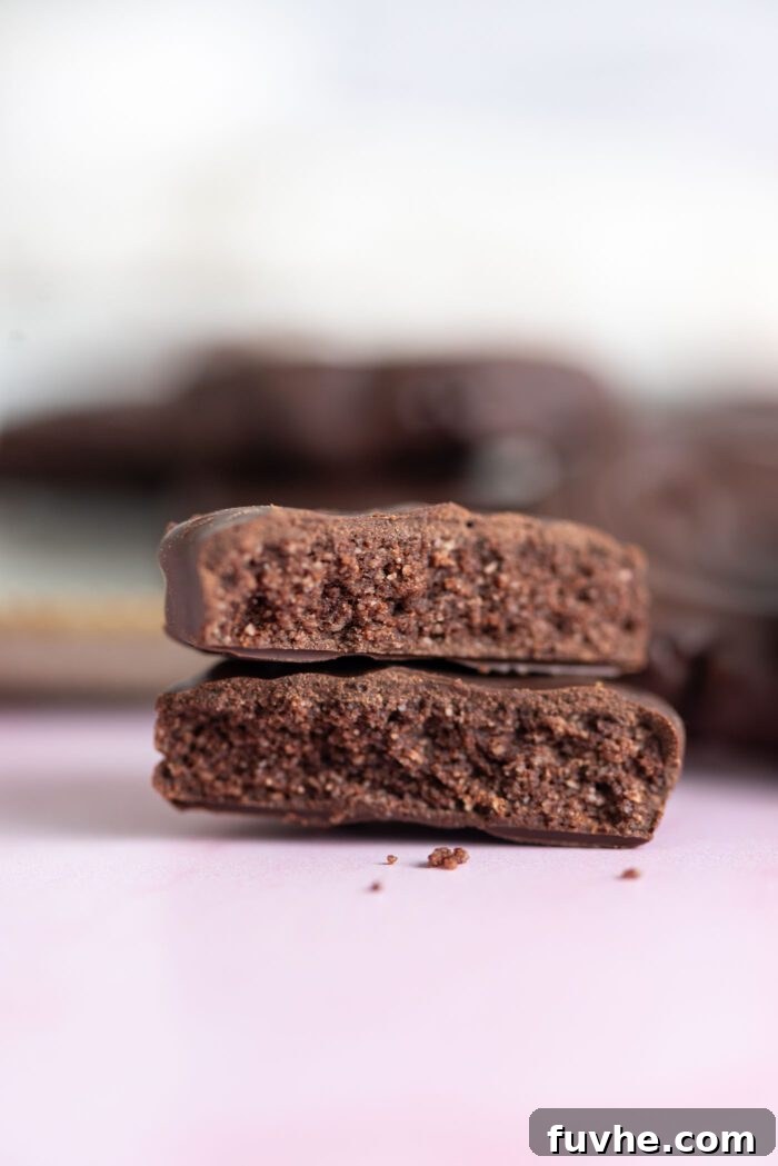 A homemade copycat Thin Mint cookie broken on half with the pieces stacked on one another so you can see the texture of the cookie inside the chocolate coating. 