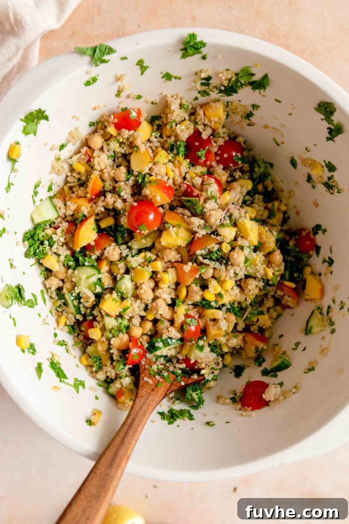 Summer quinoa salad with nectarine, chickpeas, tomato, herbs and corn in a large mixing bowl with a wooden spoon.