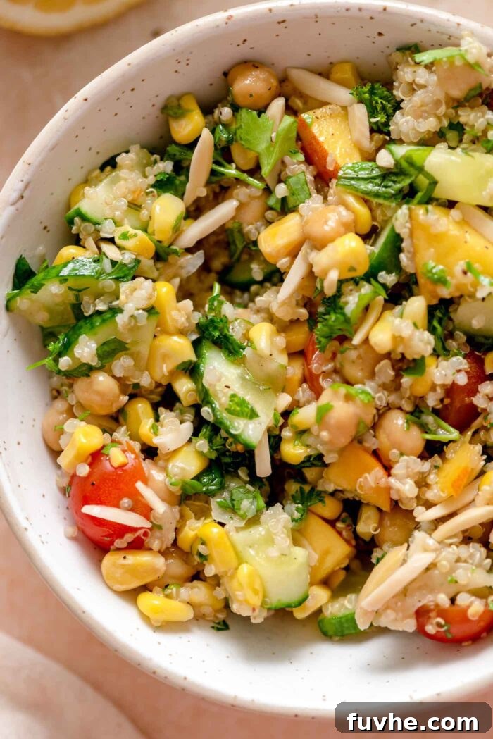 Quinoa salad with tomato, corn, nectarine, chickpeas, fresh herbs and slivered almonds in a bowl.