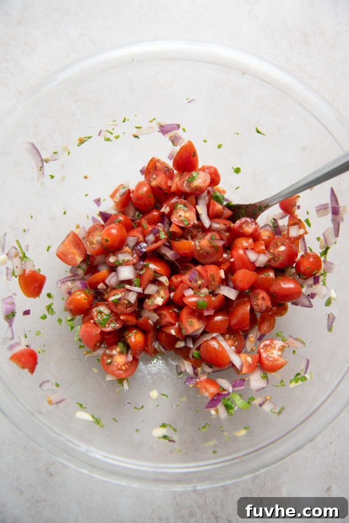 Bowl of chopped cherry tomatoes mixed with fresh parsley, red onion, and minced garlic, marinating.