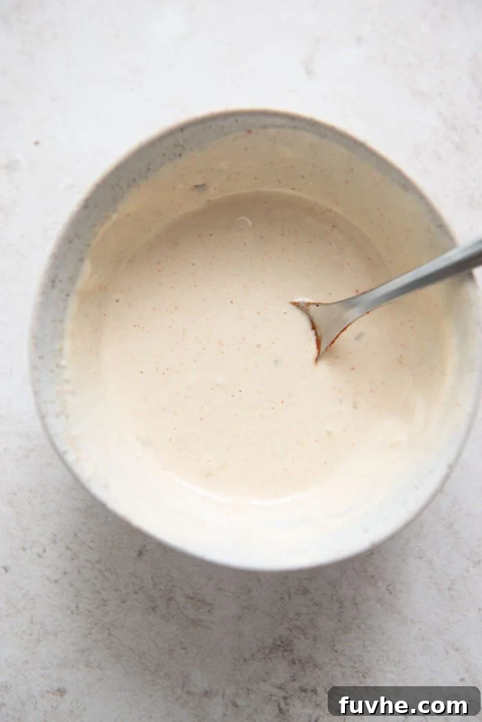 Small dish of creamy garlic tahini sauce with a spoon, showing its smooth consistency.