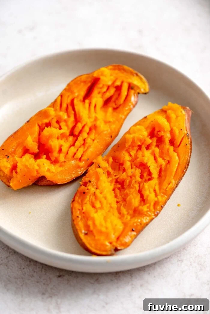 Two halves of a perfectly baked sweet potato on a plate, cut-side up and fluffed.