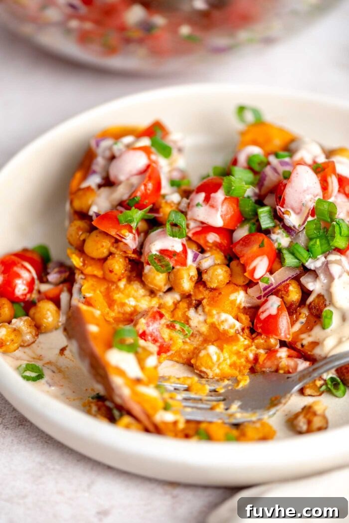 A fork on a plate of baked sweet potatoes stuffed with vibrant tomatoes, fresh parsley, and spiced chickpeas, ready to be enjoyed.