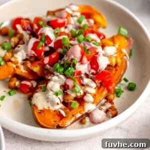 Two baked sweet potato halves topped with chickpeas, cherry tomatoes, parsley and tahini sauce.