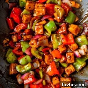 Tofu cubes with chopped pepper and onions in sauce in a wok.